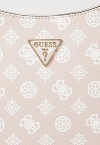 Hellrosa synthetische Handtasche mit weißem Logomuster, strukturierter Oberfläche und einer goldfarbenen dreieckigen Logoplatte mit dem Schriftzug "GUESS".