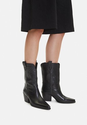 Schwarze Cowboy-Stiefel aus Leder mit spitzen Zehen, schrägen Blockabsätzen und dekorativen Nähten. Zuglaschen oben für leichtes Anziehen.