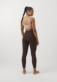 Leggings castanhos e um soutien desportivo rosa claro, exibindo um design ajustado com textura suave e um detalhe nas costas estilo racerback.