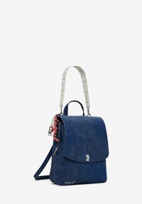 Navyblauer Rucksack mit geprägten floralen Designs, silberner Hardware und einem abnehmbaren Griff, verziert mit Nieten und einem roten Charm.