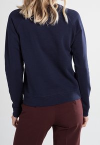 Granatowa bluza z okrągłym dekoltem i ściągaczem u dołu. Posiada rękawy typu raglan oraz miękką, gładką fakturę, zestawiona z bordowymi spodniami.