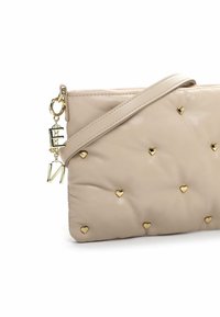 Borsa a molla in pelle beige con design trapuntato, caratterizzata da accenti d'oro a forma di cuore e una catena dorata con charm a forma di lettere. Inclusa una tracolla regolabile.