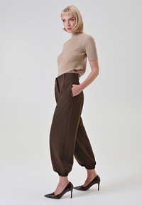Top a maniche corte beige a costine, pantaloni marroni a righe sottili a vita alta con elastici alle caviglie, e décolleté nere lucide con punta affilata.