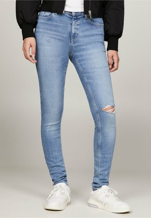 Lyseblå skinny jeans med en lille revne på højre knæ, båret med hvide sneakers og en sort jakke.