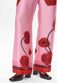 Pantaloni larghi rosa con motivo floreale rosso, caratterizzati da dettagli neri e un orlo a righe. Abbinati a scarpe con tacco a blocco lucide.