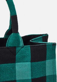 Sac en toile à carreaux verts et noirs, avec une forme structurée et des poignées doubles, présentant un motif tissé texturé et un intérieur non doublé.