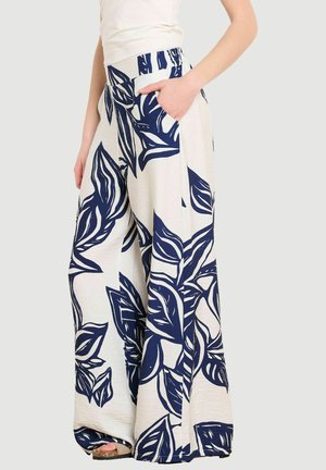 Laiade lahtiste jalgadega kreemivärvi püksid suure tumesinise lehemustriga, küljetaskutega, kandja peab ühte kätt taskus ja jalas on nähtavad beežid sandaalid.