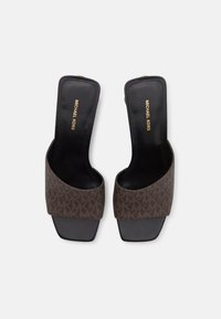 Mules à talons bruns avec un dessus en tissu à motifs et une semelle intérieure en cuir noir. Design à bout carré avec une finition lisse. Marque dorée à l'intérieur.