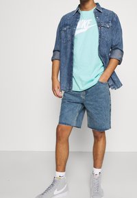 Jeansskjorta, ljusblå T-shirt med vit logo, blå denimshorts, grå högskurna sneakers, avslappnad passform, synlig sömnad och fransade kanter.