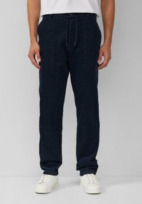 Marineblau tapering Hosen aus weichem Stoff, mit einem Kordelzugbund, seitlichen Taschen und subtilen Steppdetails. Getragen mit weißen Sneakers.