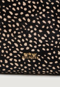 Fekete és barna foltos szőrmés anyag, melyen egy arany "Tommy Hilfiger" logó található fekete háttérrel. Figyelemre méltó textúra, sima felülettel.