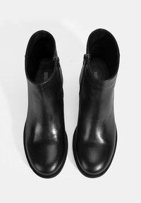 Une paire de bottines en cuir noir avec des fermetures éclair sur le côté, vues de dessus sur un fond blanc.