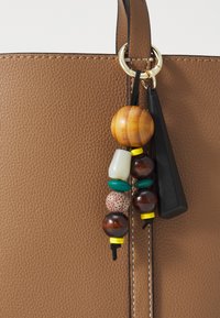 Braune, strukturierte Leder-Tote mit einem dekorativen Charm, der aus Holz-, Keramik- und Metallperlen in verschiedenen Farben besteht und mit einem schwarzen Band befestigt ist.