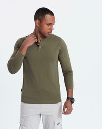 Man med olivgrön långärmad henley-tröja och ljusgrå cargobyxor, tittar ner och rör vid kragen med vänster hand.