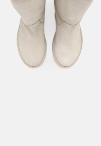 Botas de ante beige hasta la rodilla con punta redondeada y mínimos detalles de costura. La suela es de color claro con un acabado ligeramente texturizado.