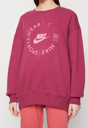 Sweatshirt oversize bordeaux avec col ras du cou, arborant un grand logo Nike blanc et une impression graphique. Fabriqué en mélange de coton doux.