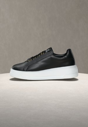 Zapatilla negra de cuero bajo con suela plataforma blanca, ojales dorados y "Love Moschino" grabado en el lateral, exhibida sobre una superficie neutra.