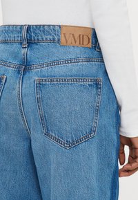 Μπλε τζιν παντελόνι από denim με κλασική εφαρμογή, ορατές ραφές, δύο πίσω τσέπες και μια ταμπέλ�α από δέρμα σε ταμπά χρώμα με ανάγλυφο το λογότυπο "VMD" στη μέση.