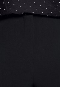 Zwarte broek met een naadloos frontontwerp en een gladde textuur; gemaakt van een lichtgewicht, rekbaar materiaal. Gepaard met een donker shirt met witte stippen.