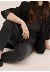 Blazer noir sur un haut gris foncé texturé, associé à un jean gris foncé avec un ourlet effiloché. Des chaussures noires complètent la tenue.