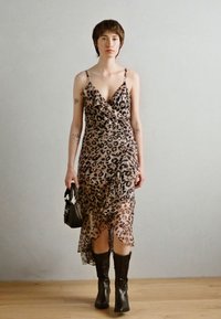 Oblačilo iz prosojnega materiala z leopardjim vzorcem, z obliko ovitka in nabrano spodnjo obrobo. Črne škornje do kolen. Manekenka drži majhno črno torbico.
