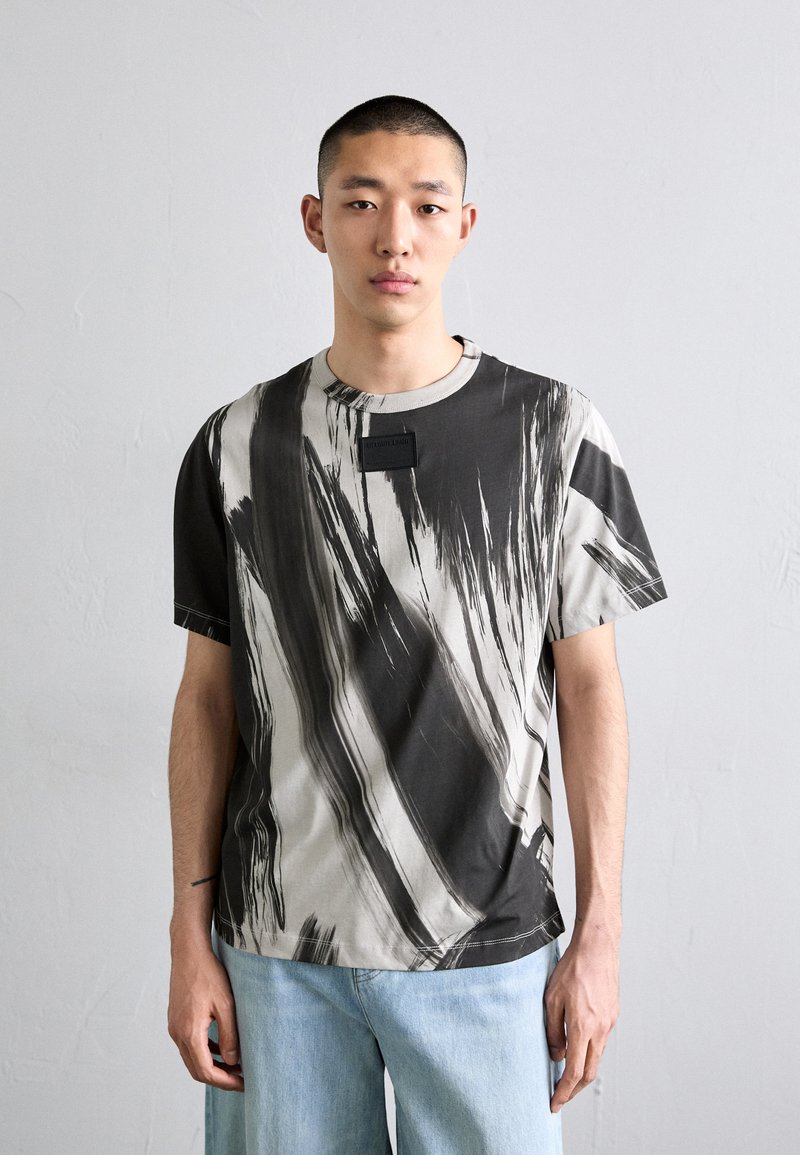 Fekete és szürke absztrakt csíkos rövid ujjú póló, pamut anyagból, kerek nyakkivágással, testhezálló kialakítással, kis címkével a mellkason.