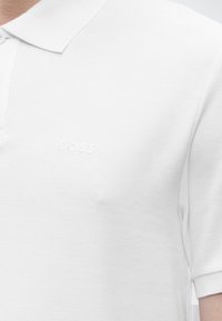 Polo blanc texturé avec petit logo « BOSS » embossé sur la poitrine gauche, manches courtes et col à revers avec boutons.