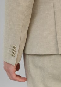 Beige kostuumjacket met een gestructureerde stof, vier knoopaccenten aan de mouwen en een schone, op maat gemaakte silhouet.