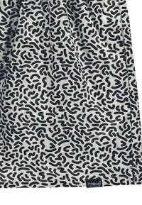Tessuto a motivi con un design ondulato nero su uno sfondo chiaro, con una piccola etichetta del marchio nell'angolo in basso.