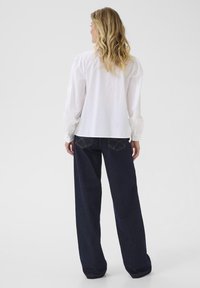 Vit långärmad skjorta med puffärmar, kombinerad med mörkblå vida jeans som har bakfickor och blå sömmar.