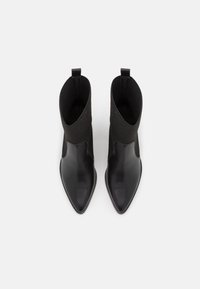 Botas de tobillo de cuero negro con una parte superior de punto acanalado, punta afilada y tira para poner. Textura suave y diseño elegante.