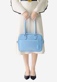 Bolso de cuero azul claro con dos asas, de forma rectangular, que presenta herrajes dorados y un bolsillo con cremallera. Superficie lisa con detalles de costura.