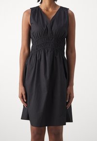 Svart ärmlös klänning med V-ringning, som har en elastisk midja, en utsvängd kjol och sidofickor för ökad rörlighet.