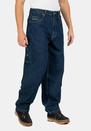 Baggy dark blue denim jeans with a side pocket, featuring a classic five-pocket design and a loose fit, paired with brown hiking boots.