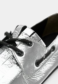 Ασημένιο παπούτσι με κορδόνια, με υφή και γυαλιστερή επιφάνεια, μαύρα κορδόνια και σκούρα οπές για τα κορδόνια. Διαθέτει κλασικό σχέδιο με ελαφρώς στρογγυλεμένη μύτη.