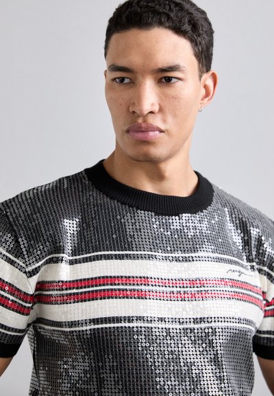 T-shirt noir et argent à sequins avec des rayures horizontales rouges et blanches. Col rond, manches courtes et sequins texturés créent un effet scintillant.