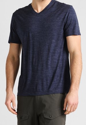 Homme portant un T-shirt à manches courtes bleu marine à col en V et un pantalon cargo vert olive, debout devant un fond clair.