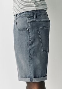 Herren-Jeansshorts in Blau mit aufgerolltem Saum, Fünf-Taschen-Design und strukturierter Stoffqualität, die einen geraden Schnitt und eine mittelhohe Taille zeigen.