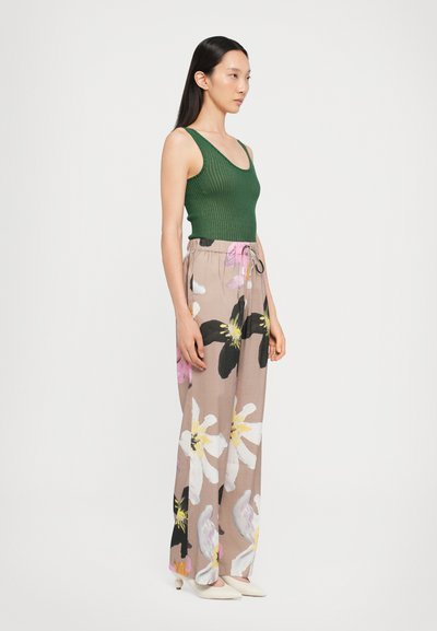 Canottiera verde a coste abbinata a pantaloni larghi beige con stampa floreale caratterizzati da grandi fiori neri e rosa; il modello indossa scarpe con punta a stiletto bianche.