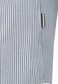 Gestreiftes Hemd aus blau-weißem Baumwollstoff, mit vertikalen Linien, einem seitlichen Etikett mit drei horizontalen Streifen in Marineblau, Braun und Creme.