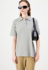 Grå bomullspolo med krage, korte ermer og liten logo. Kombinert med beige bukser og en liten svart veske.