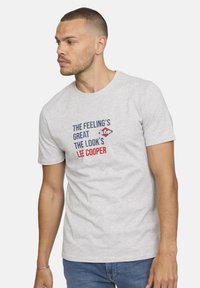 T-shirt en coton gris avec col rond, manches courtes et texte imprimé en bleu et rouge. Le design comprend le nom de la marque Lee Cooper.