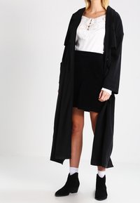 Mustat pitkät takki, valkoinen paita pitsidetaljilla, mustat hameet ja mustat nilkkurit. Asusteessa on yksinkertaisia, selkeitä linjoja ja erilaisia tekstuureja.