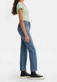 Top corto a maniche corte verde a coste abbinato a jeans dritti blu a vita alta e sneaker nere alte. Focus su vestibilità casual e tessuto.