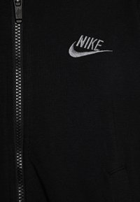 Fleece com fecho éclair preto, feito de um tecido suave, apresentando um logo da Nike em prata bordado no lado esquerdo do peito e um fecho texturizado.