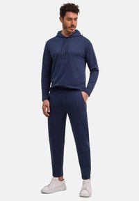 Dunkelblaues Kapuzensweatshirt mit gerippter Textur, kombiniert mit passenden schmal geschnittenen Hosen. Das Model trägt weiße Sneakers für einen lässigen Look.
