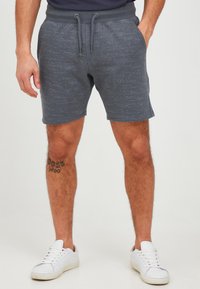 Gray textured shorts with a drawstring waist, featuring a subtle striped pattern. Paired with white sneakers, displaying a tattoo on the leg.