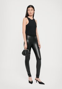 Mustat ilmaõlaga särk, mille juurde on sobitatud läikivad mustad leggings, mustad kõrged kontsad ja väike, kokku volditud must käekott. Siledad tekstuurid.