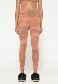 Leggings mimetici in tonalità di rosa e marrone; design aderente con vita alta; texture liscia; abbinati a sneaker nere.