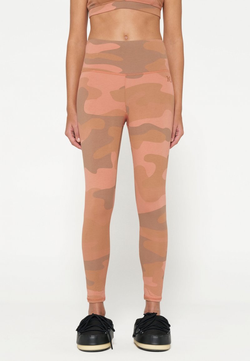 Leggings mimetici in tonalità di rosa e marrone; design aderente con vita alta; texture liscia; abbinati a sneaker nere.